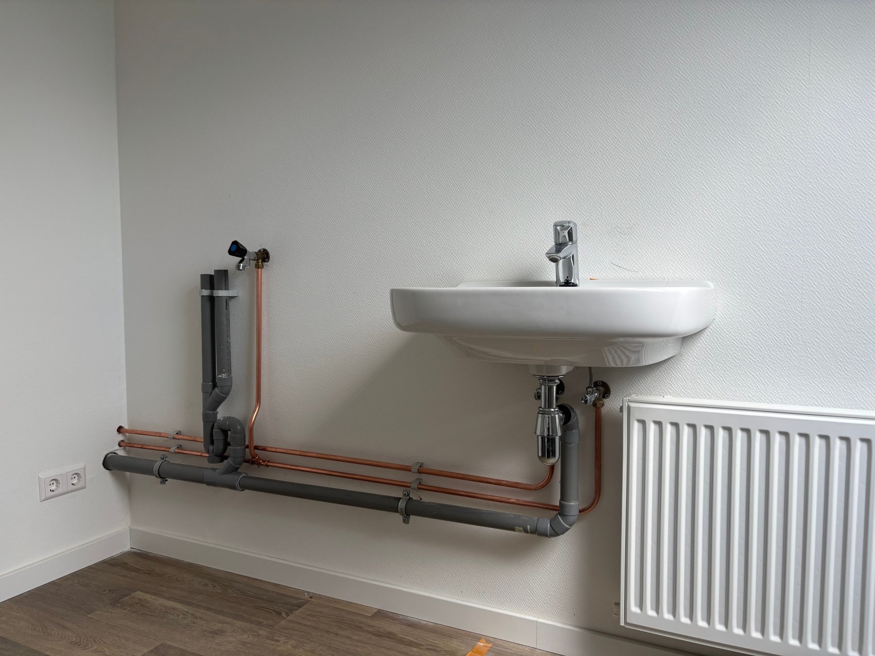 Nieuwe wastafel met strak leidingwerk en een witte paneelradiator